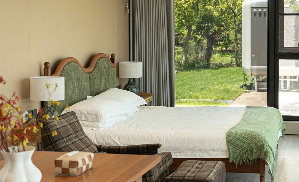 Cozy capsule house bedroom interior with a lush garden view, featuring a stylish bed, elegant lamps, and a welcoming atmosphere.