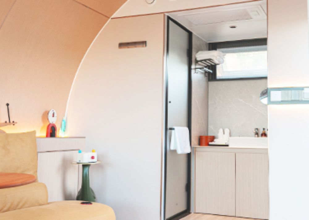 Modern capsule house interior showcasing a compact bathroom with a shower, marble countertop, and cozy living area.