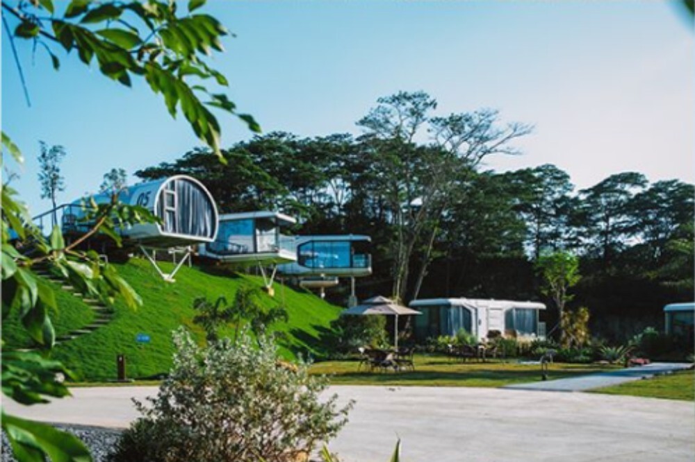 Eco-friendly capsule house resort with multiple units terraced on a verdant hillside, surrounded by dense forest and walking paths.