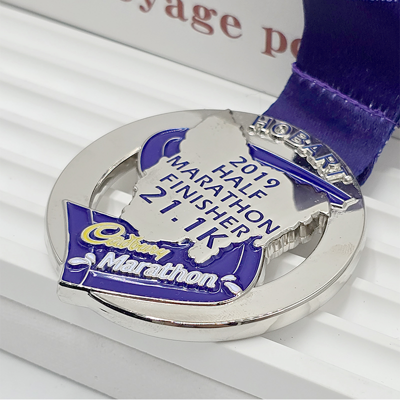 Silver and purple two-tone metallic medal for the Hobart Half Marathon finisher, 21.1K circular relief, Cadbury co-branded race collectible.