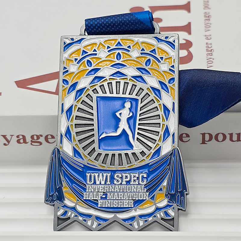 Silver, blue, and yellow color-blocked metal medal, UWI SPEC International Half Marathon finisher commemorative item, mosaic-patterned runner relief, Caribbean race collectible.