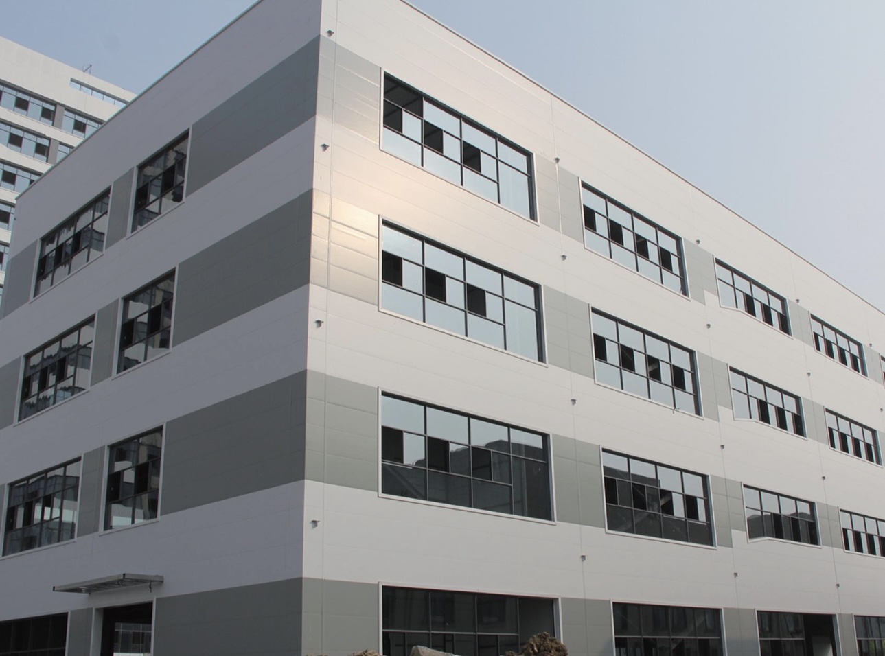 Multi-story factory building with grey-and-white striped color-coated steel cladding