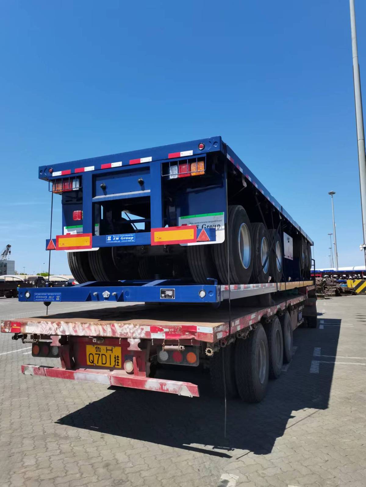 53FT tri axle flatbed semi trailer at seaport for overseas delivery, secured on container chassis with factory packaging and bulk trailer shipping operation