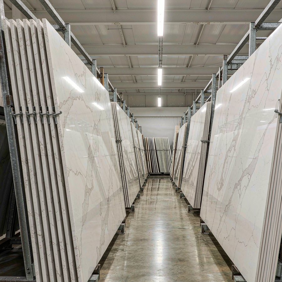 Large-format polished engineered quartz slab standing on an A-frame rack beside thin porcelain slabs in a stone warehouse, showing the quartz vs porcelain thickness difference