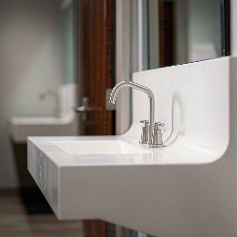 1790236833961656738257330176.jpg One-piece solid surface vanity top with an integrated coved backsplash and basin in a commercial washroom, formed with no visible joints